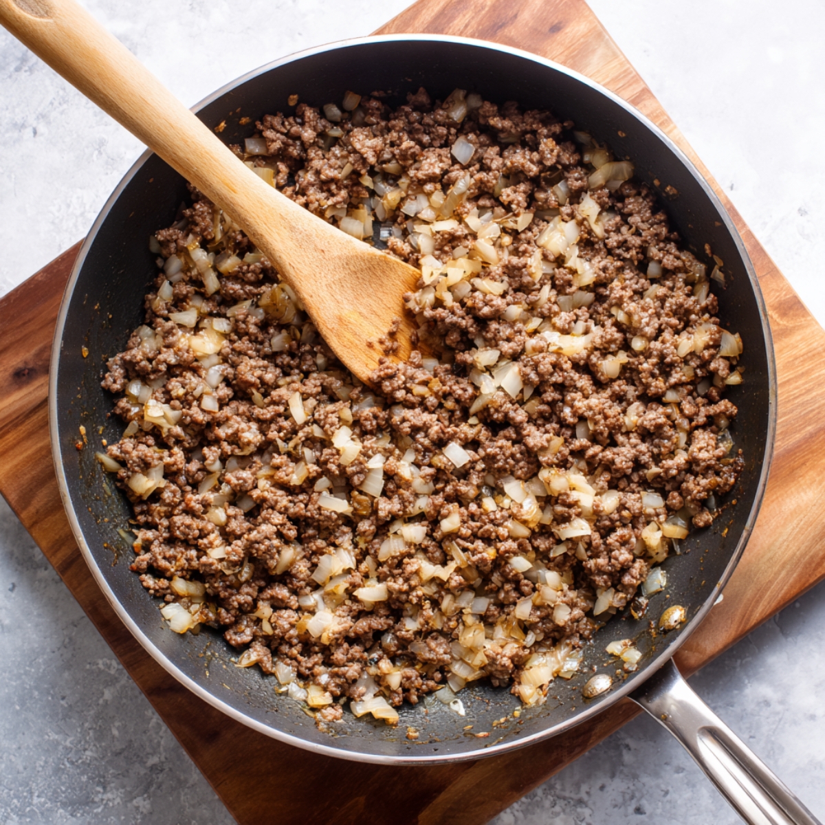 Skillet with browned ground beef and onions, stirred with a wooden spoon, forming the base for the cabbage roll filling.