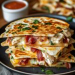 A stack of grilled chicken bacon ranch quesadillas, oozing melted cheese, with crispy bacon and juicy chicken inside golden tortillas, topped with chopped cilantro on a black plate.