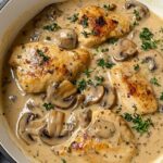 Creamy mushroom chicken with golden seared breasts in a rich garlic-herb cream sauce, topped with fresh thyme in a white skillet on a kitchen towel.