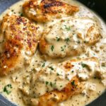 Golden seared chicken breasts in a skillet, smothered in Creamy Ranch Chicken sauce with herbs, garlic, and parsley garnish.