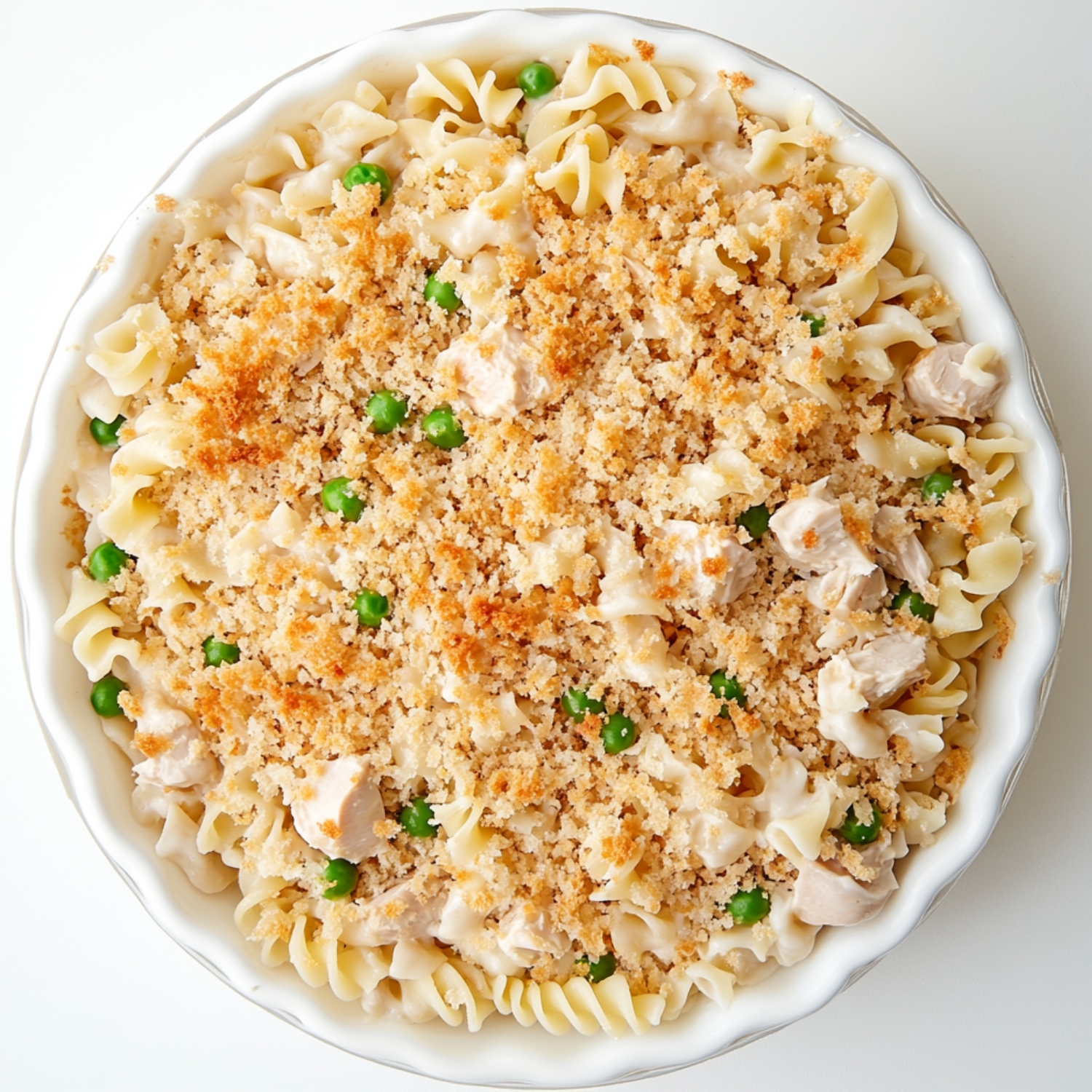 Unbaked tuna noodle casserole topped with golden breadcrumbs and peas in a white round baking dish.