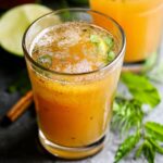 Homemade apple cider vinegar drink recipe in a glass with herbs, spices, and a fresh, golden-orange color, surrounded by lime, cinnamon, and apples.