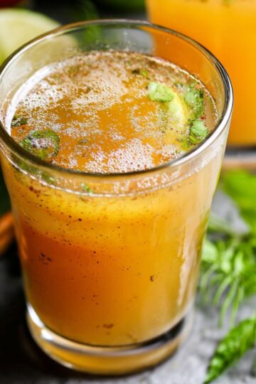 Homemade apple cider vinegar drink recipe in a glass with herbs, spices, and a fresh, golden-orange color, surrounded by lime, cinnamon, and apples.