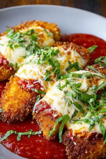 Homemade Chicken Parmesan Recipe with crispy golden cutlets, melted mozzarella, rich marinara sauce, and fresh basil on a gray plate.