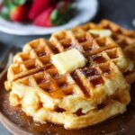 Homemade golden Waffle Recipe topped with butter and maple syrup, served on a wooden plate.