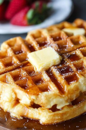 Homemade golden Waffle Recipe topped with butter and maple syrup, served on a wooden plate.