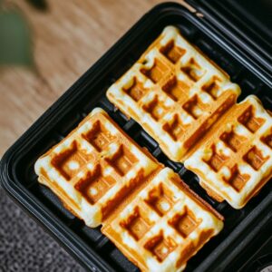 Golden homemade waffles cooking in a waffle iron, with crisp edges and light centers, just finished baking in a cozy home kitchen setting.