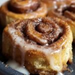Homemade sourdough cinnamon rolls with gooey vanilla glaze dripping over soft, golden-brown swirls of cinnamon sugar.