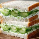 A homemade cucumber sandwich with soft white bread, thinly sliced fresh cucumbers, and a creamy spread, stacked neatly with a golden-brown crust on the outside.