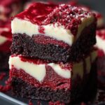 A stack of two thick Red Velvet Brownies squares with a creamy, swirled cream-cheese topping. The dense, moist brownie base is a deep mahogany red, while the smooth cream-cheese layer on top is pale ivory with dramatic red velvet streaks. Crumbly red velvet bits and a light dusting of powdered sugar cling to the edges, and you can just make out the fudgy interior and velvety texture against a dark serving platter