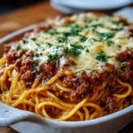 A baked spaghetti Recipe casserole topped with melted cheese and parsley, served in a white ceramic baking dish