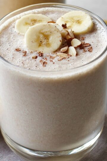 Creamy banana smoothie recipe in a glass topped with banana slices, chopped almonds, and a sprinkle of cinnamon.