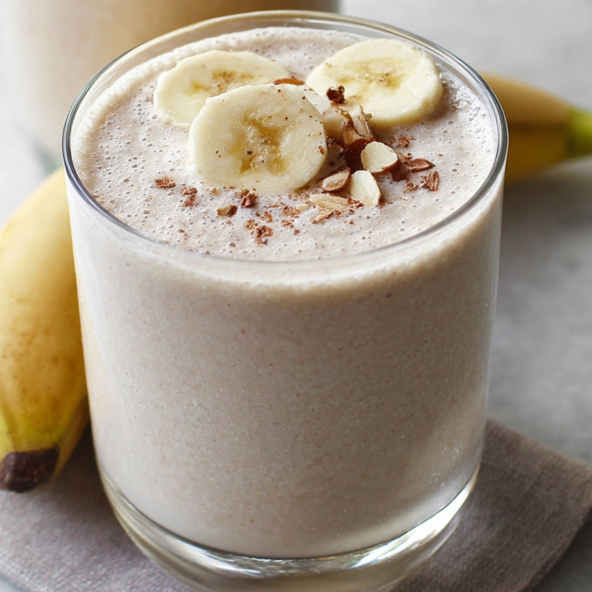 Creamy banana smoothie recipe in a glass topped with banana slices, chopped almonds, and a sprinkle of cinnamon.
