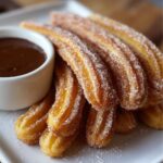 Close‑up of freshly fried churros recipe being lifted from hot oil with tongs, sugar raining down onto their ridged surfaces.