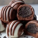Homemade Oreo truffles coated in chocolate with white and milk chocolate drizzle, served on a plate with Oreo crumbs and a rich, creamy cookie filling inside.