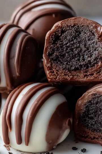 Homemade Oreo truffles coated in chocolate with white and milk chocolate drizzle, served on a plate with Oreo crumbs and a rich, creamy cookie filling inside.