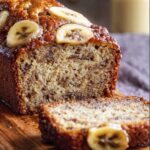 Homemade Banana Bread Recipe slices on a wooden board, with a golden crust, moist texture, and visible banana and nut pieces.