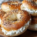Golden, homemade everything bagels filled with whipped cottage cheese bagels. Crispy on the outside, fluffy inside, with seeds and creamy filling slightly spilling out—stacked on a wooden plate in natural light.
