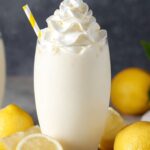 A cozy, mood-lit scene on a reclaimed wood board: a small jar of whole milk garnished with a mint sprig and a Creamy Lemonade wheel, a tall glass rimmed with condensation and filled with pale yellow creamy lemonade topped with a honey-drenched ice cube, fresh lemon halves and a honey dipper arranged artfully around, shallow depth of field, warm golden-hour light, hyper-realistic food styling shot