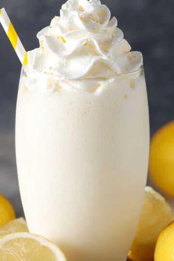 A cozy, mood-lit scene on a reclaimed wood board: a small jar of whole milk garnished with a mint sprig and a Creamy Lemonade wheel, a tall glass rimmed with condensation and filled with pale yellow creamy lemonade topped with a honey-drenched ice cube, fresh lemon halves and a honey dipper arranged artfully around, shallow depth of field, warm golden-hour light, hyper-realistic food styling shot