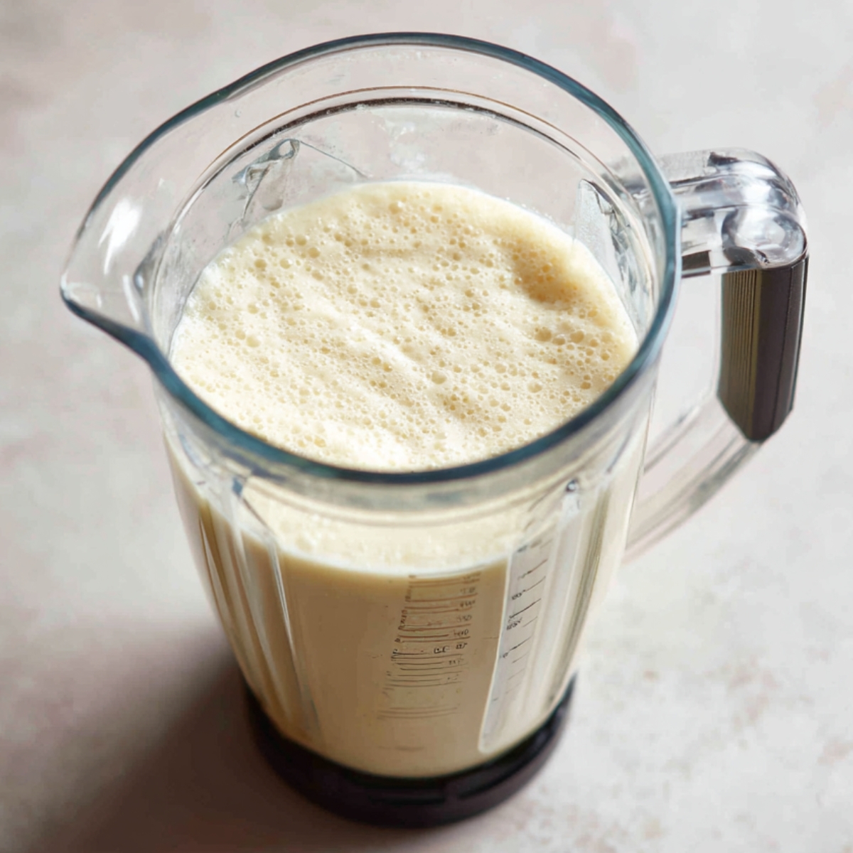 Freshly blended banana smoothie in a clear blender pitcher, showing a light and frothy texture.