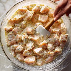 “A bright close‑up overhead view of a clear glass bowl on a white marble countertop, containing creamy ranch dressing swirled with minced garlic, a drizzle of olive oil, fresh lemon juice, and a sprinkling of cracked black pepper; a stainless steel whisk mid‑stir, textures and colors in sharp focus under soft daylight