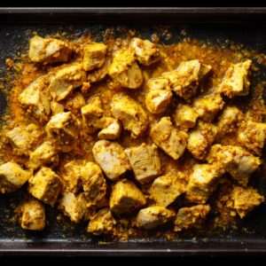 Diced yellow onion being scraped from a white skillet into a bubbling orange‑cream sauce on a sleek induction cooktop.