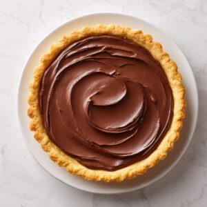 Overhead view dyal golden pie crust ʿla white plate, me3mra b chocolate cream msayyeb b strokes naʿbin ʿla marble background.