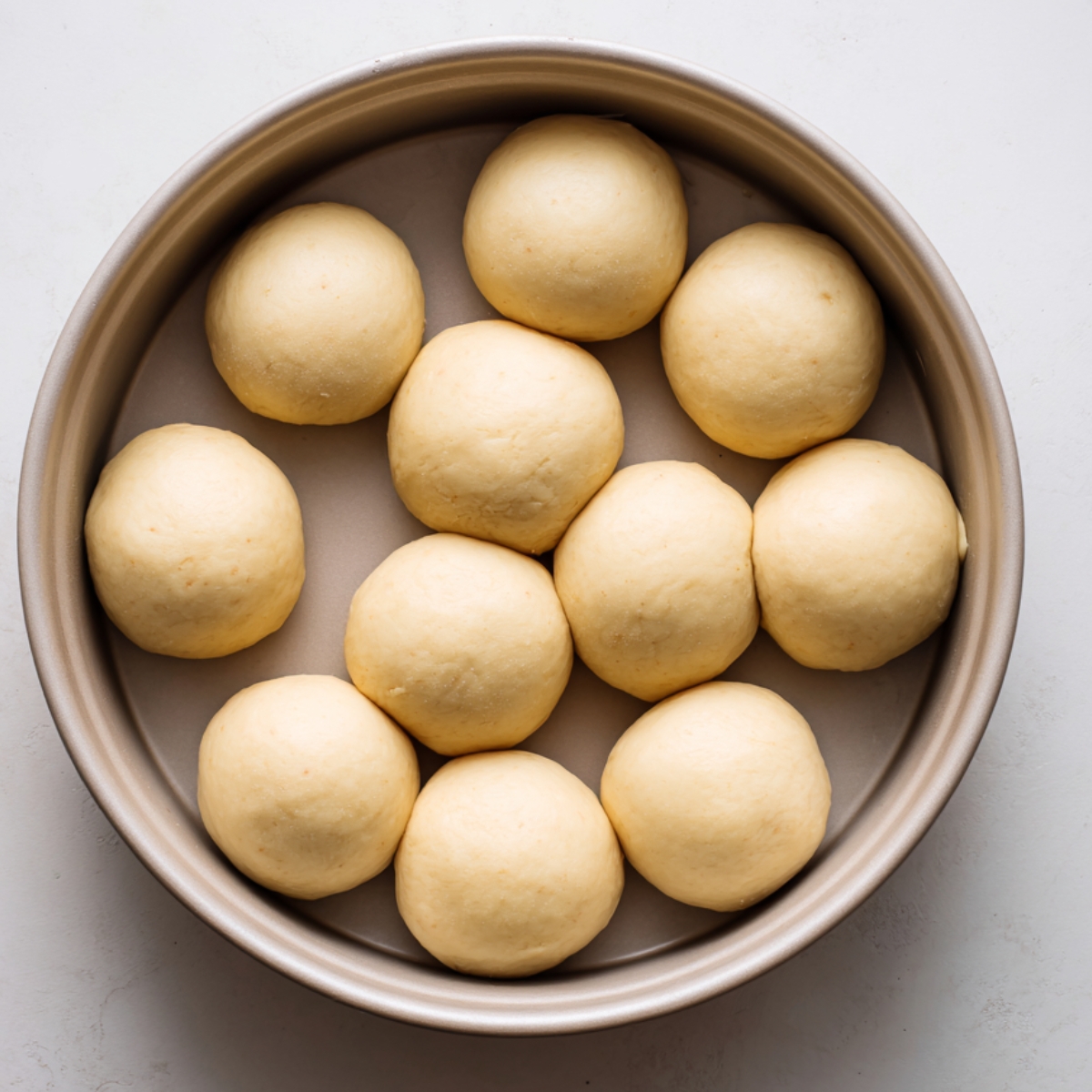 Evenly spaced dough balls in a greased round pan before the second rise.