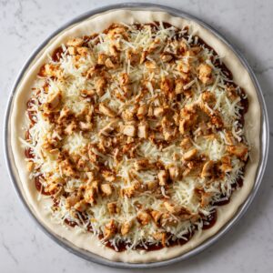 Pizza raw mghatta b jibna mozzarella w BBQ chicken mshat 3la dough.