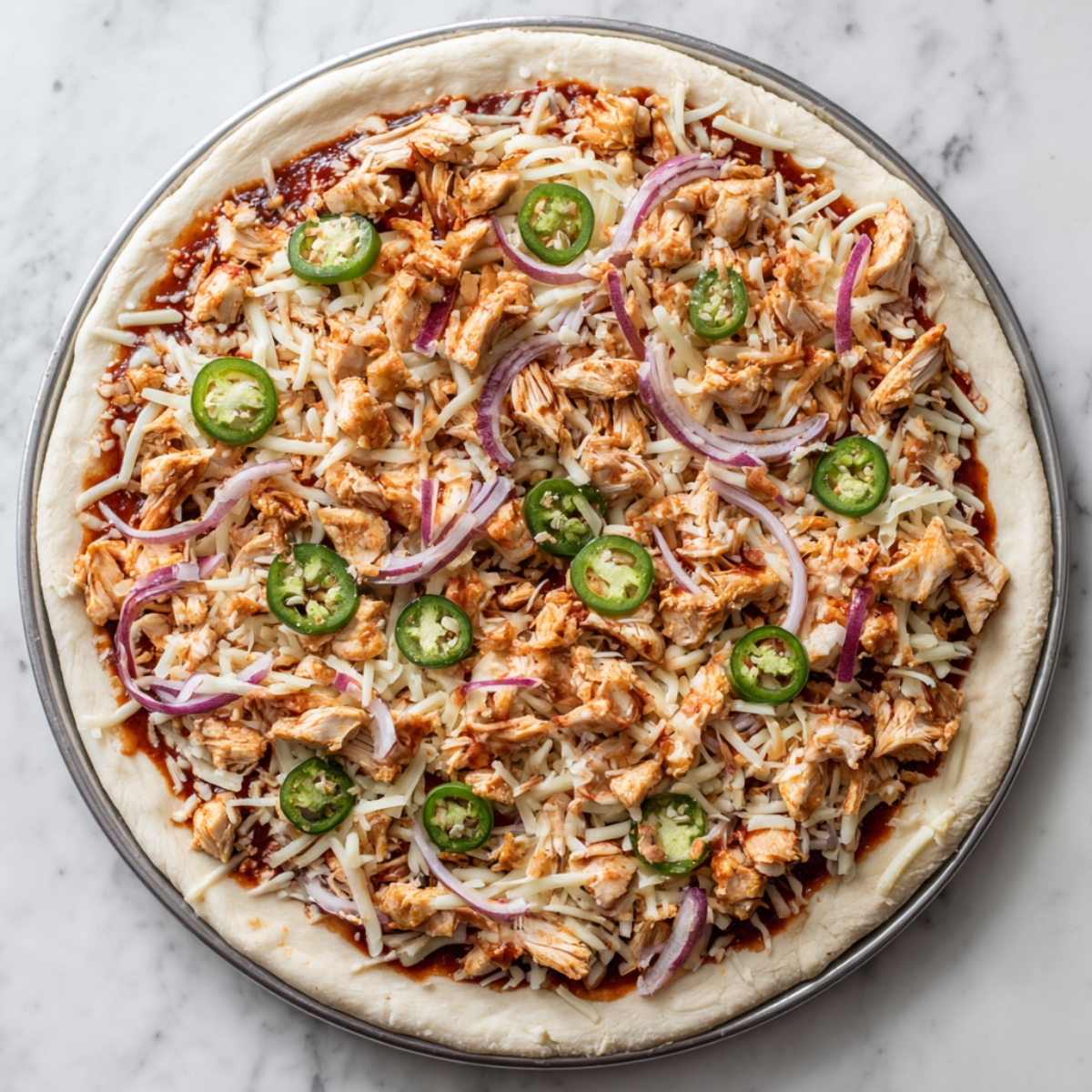 Pizza raw mghatta b BBQ sauce, jibna mozzarella, BBQ chicken, jalapeño, w bassla 7amra mfrsha 3la dough.