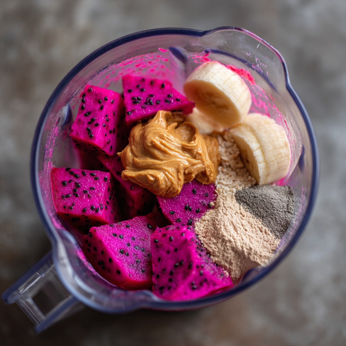 A blender filled with chopped dragon fruit cubes, banana slices, peanut butter, and various powders.