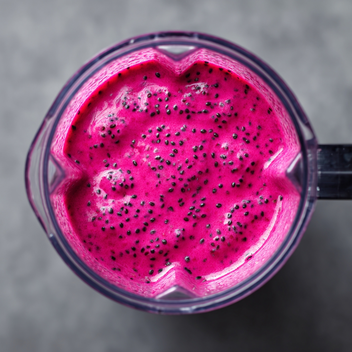 A blender jar filled with a creamy, bright pink smoothie, with visible seeds floating on the surface.
