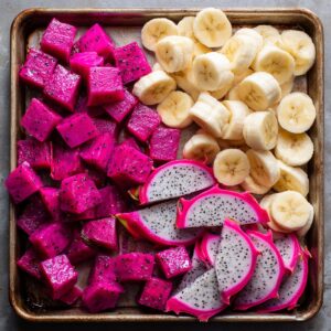A tray filled with chopped dragon fruit cubes and banana slices, with some whole dragon fruit still on the tray.