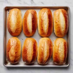 “A golden-crusted French dip sandwich on a white plate, filled with tender roast beef and melted cheese, accompanied by a white ramekin of dark au jus in soft natural light.”