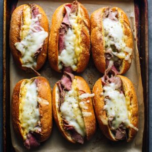 “Thinly sliced roast beef pieces submerged in dark, seasoned au jus inside a pale saucepan atop a black induction cooktop, the meat gently poaching in the savory broth.”