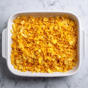 Overhead shot of the white ceramic pan showing a bubbling, golden-orange cornflake-and-cheese crust crisped at the edges.