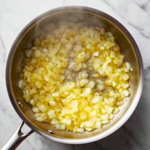 Top‑down image of a stainless‑steel soup pot on a marble countertop, brimming with creamy potato soup dotted evenly with finely chopped herbs, paprika, and black pepper
