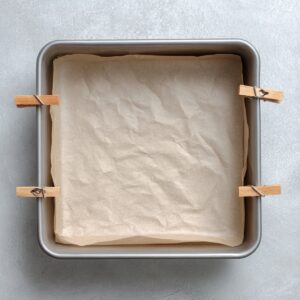 Close-up of the red velvet batter evenly spread in the prepped parchment-lined pan, the unblemished, glossy surface reflecting soft natural light.