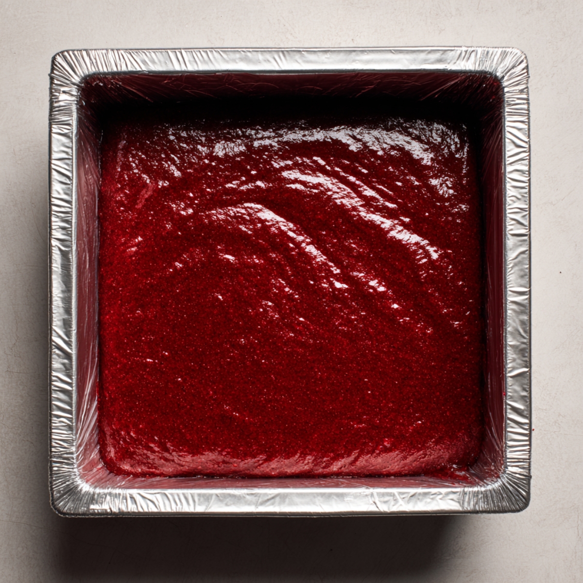 Top-down shot of a small glass bowl on the same countertop, containing ivory cream-cheese swirl filling with a wooden spoon coated in the creamy mixture, the light catching its velvety surface.
