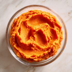 Top-down view of a white rectangular baking dish on a marble countertop, the sweet potato layer fully covered by a raw pecan streusel topping