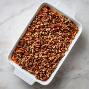 Overhead of a small clear glass bowl on marble, packed with a coarse streusel mix of chopped pecans, brown sugar, flour, and butter crumbs.