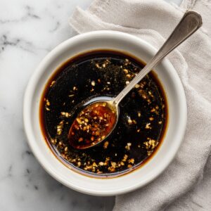 Six golden-brown teriyaki-glazed chicken thighs arranged irregularly on a clean white cutting board, with sauce droplets around them, photographed from above.