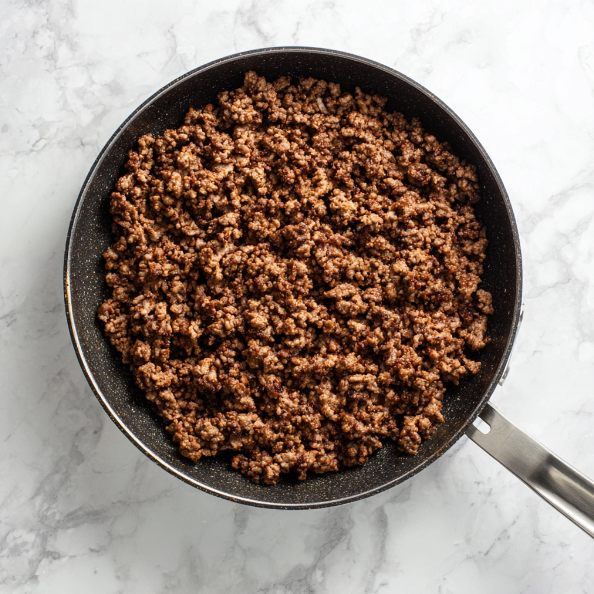 Top-down photo of a large nonstick skillet filled with evenly browned, crumbled ground meat, sitting on a white marble countertop.