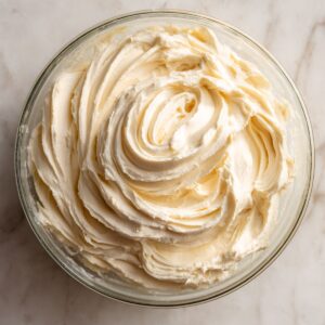 A glass bowl filled with freshly whipped cream cheese mixture, swirled to perfection with soft peaks, sitting on a marble surface in a home kitchen.