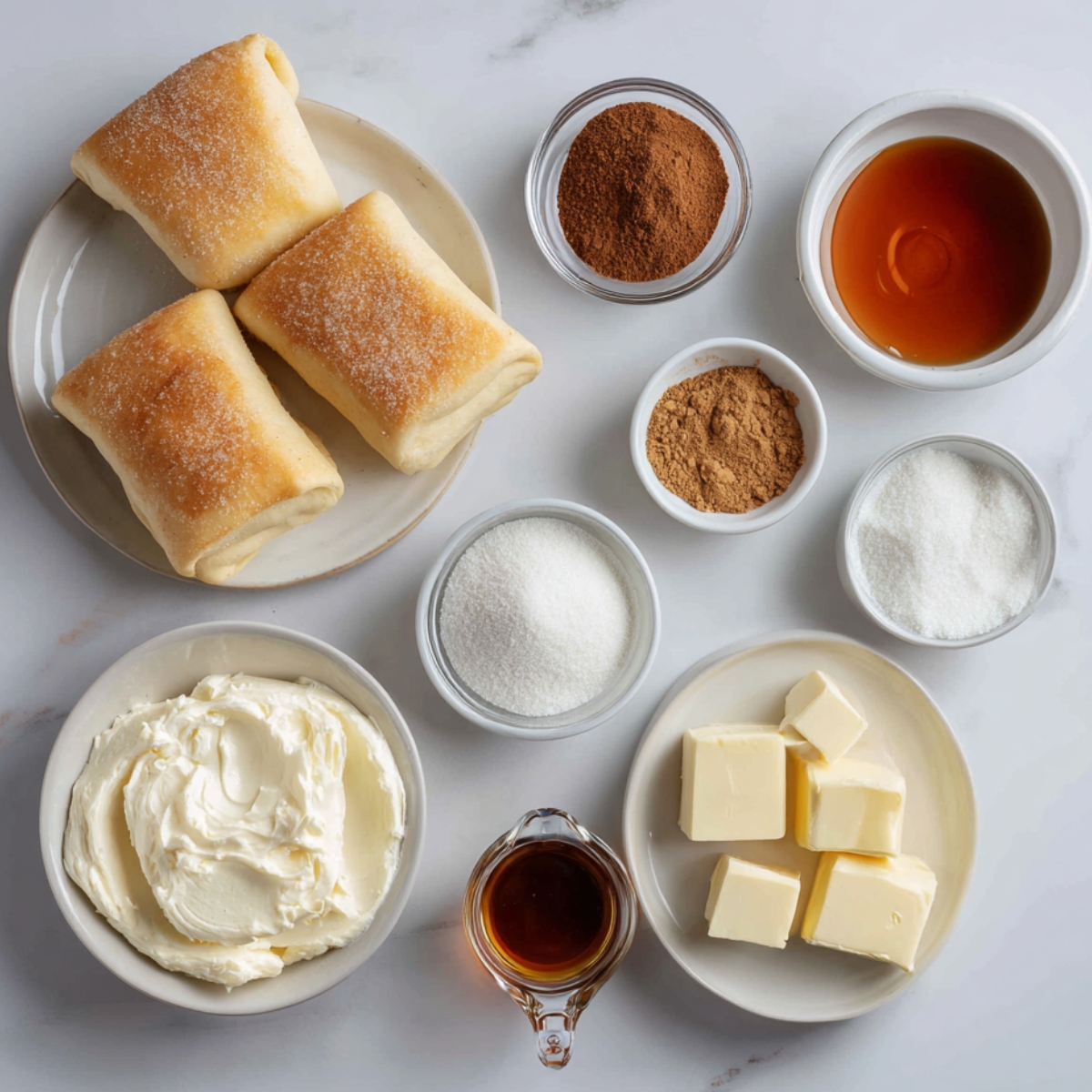 An organized flat lay of sopapilla cheesecake ingredients: crescent dough pieces, cream cheese, cubed butter, cinnamon, sugar, brown sugar, vanilla, and honey, arranged on a clean white surface.