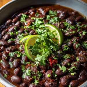 Serving bowl of cooked black beans recipe topped with fresh cilantro and lime slices