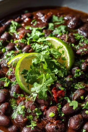 Serving bowl of cooked black beans recipe topped with fresh cilantro and lime slices
