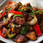 Spicy black pepper chicken stir-fry with green and red bell peppers, onions, and herbs served with steamed white rice on a plate