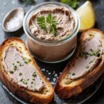 A jar of Chicken Liver Pate recipe garnished with parsley, served with two slices of toasted bread spread with pâté, with the word “PATE” spelled in wooden letters in the background.